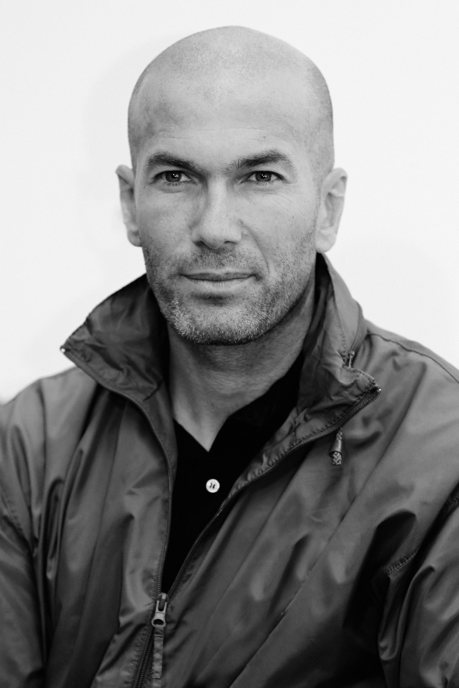 Retrato en blanco y negro de Zinedine Zidane con una chamarra, mirando de frente a la cámara.