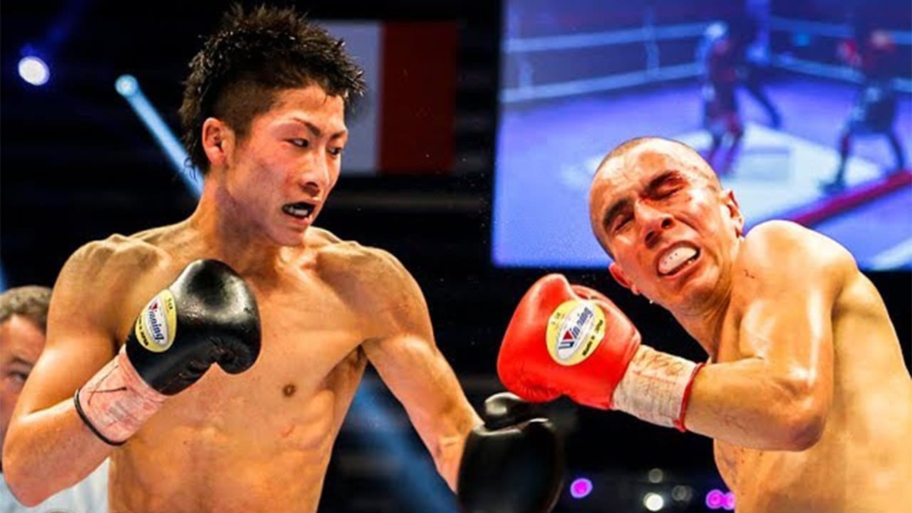 Dos boxeadores sin camiseta se enfrentan sobre el ring, uno con guantes negros lanzando un golpe y el otro con guantes rojos recibiendo el impacto.