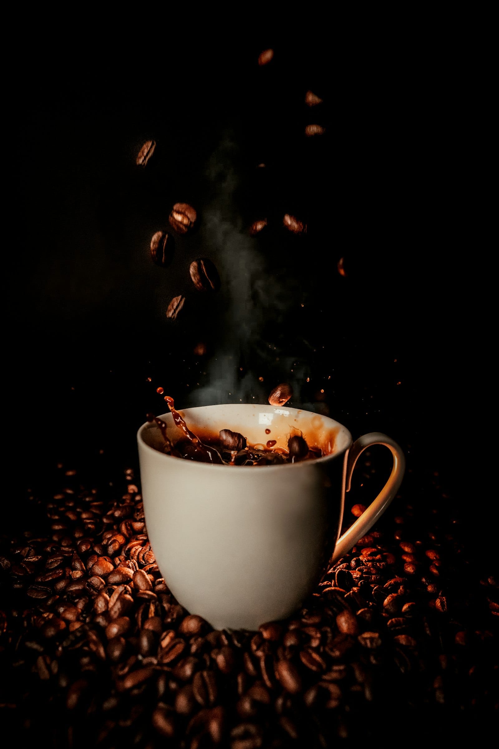 Una taza de café humeante con granos tostados esparcidos a su alrededor sobre una superficie oscura.