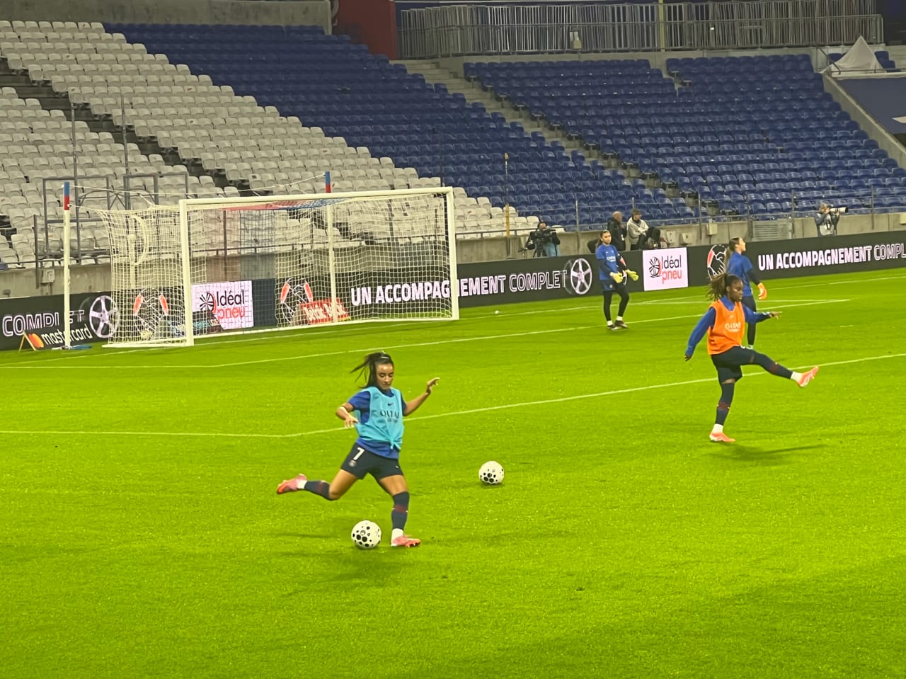 Futbolistas con petos de entrenamiento patean balones durante un calentamiento en un estadio con las gradas casi vacías.