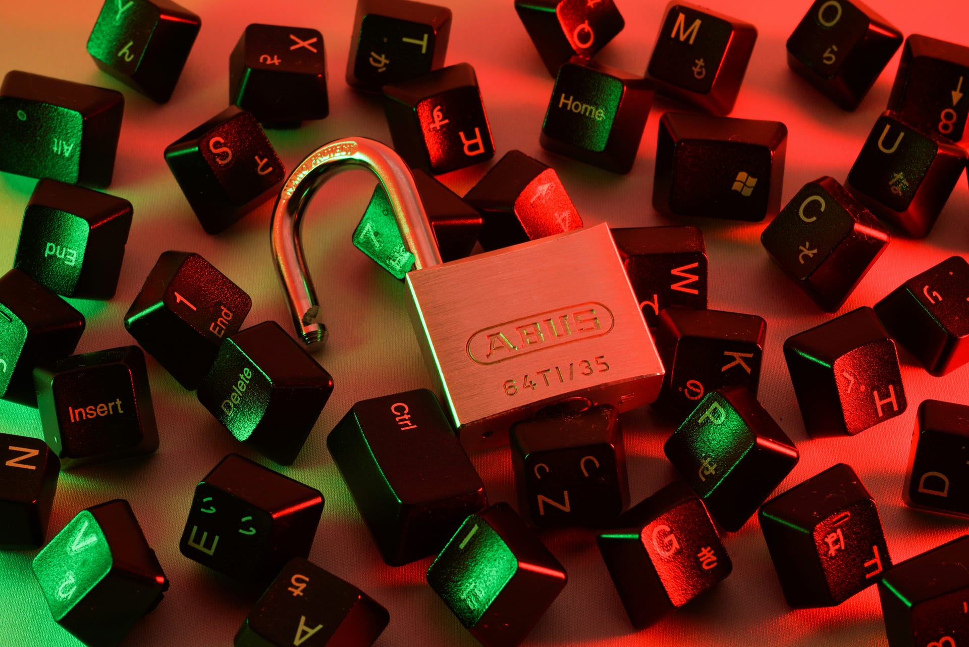 Un candado abierto entre teclas de teclado dispersas, iluminado con luces rojas y verdes.