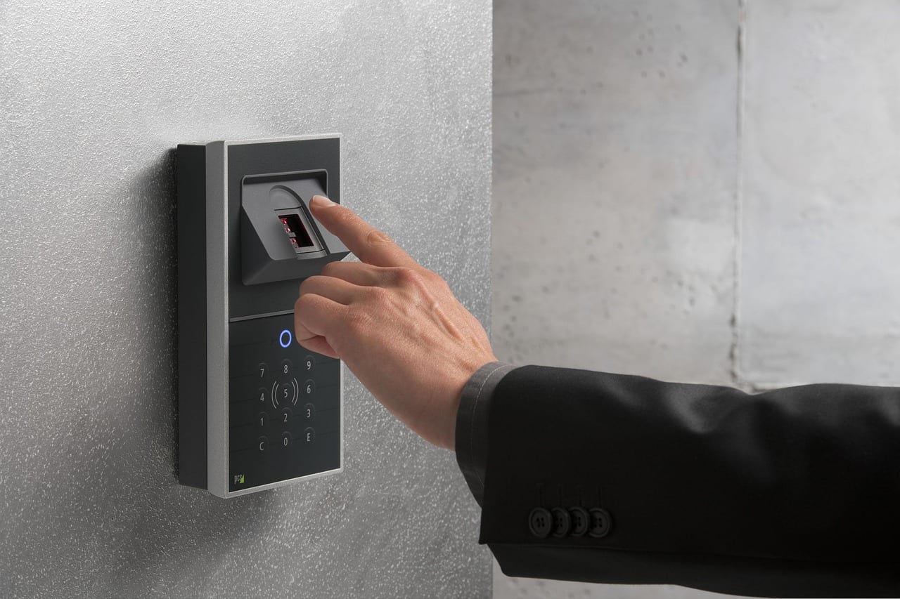 Un hombre de traje presiona con el dedo un lector de huella digital instalado en una pared.