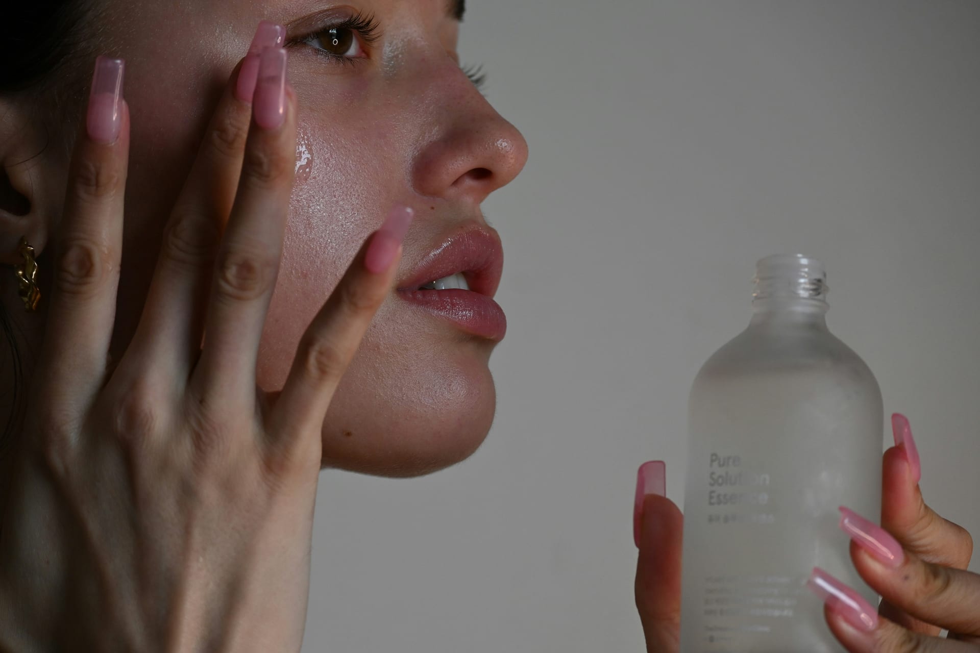 Una persona se aplica un producto de cuidado facial en la mejilla frente a un frasco de vidrio.