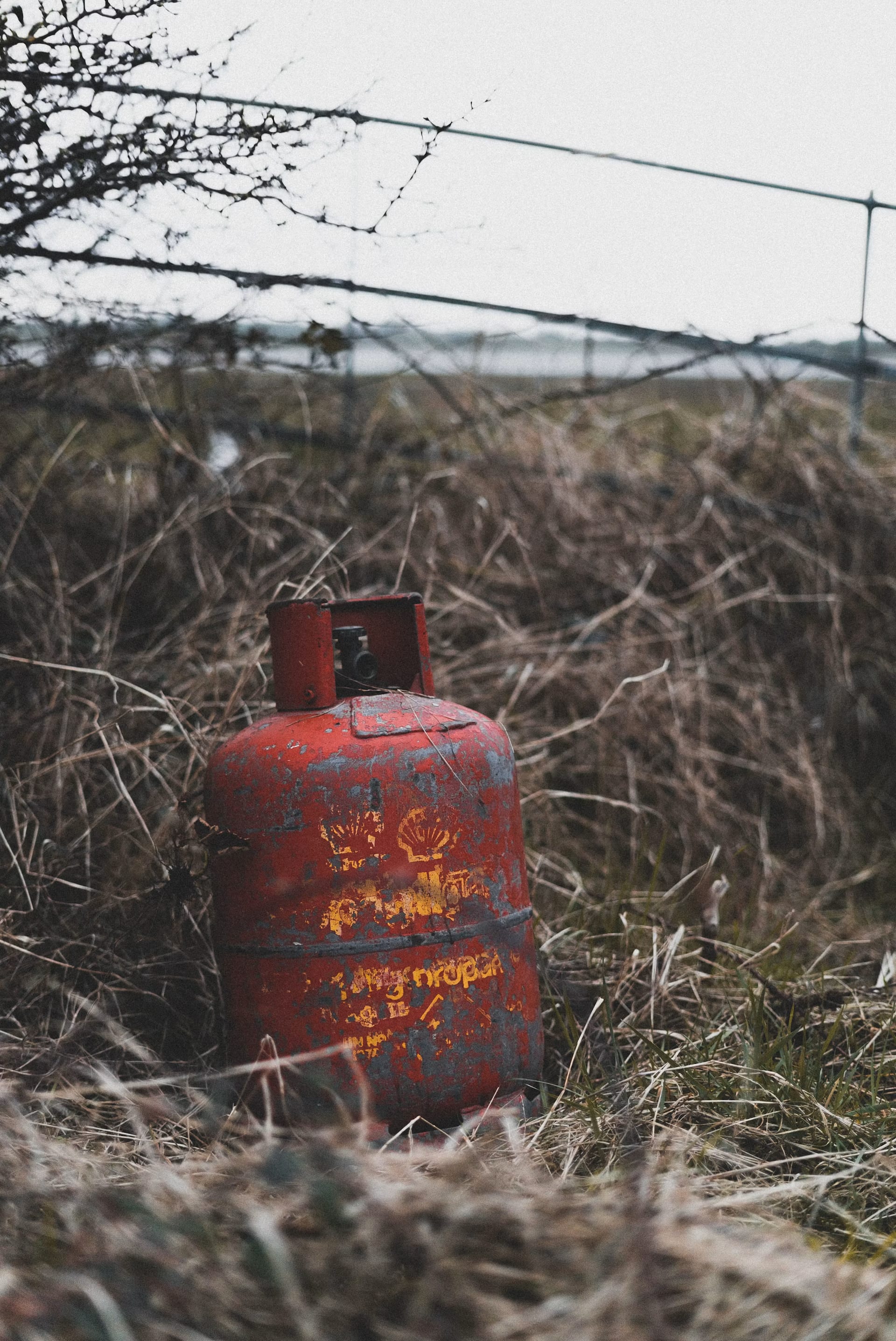 Un tanque cilíndrico de gas color rojo colocado sobre pasto al aire libre.