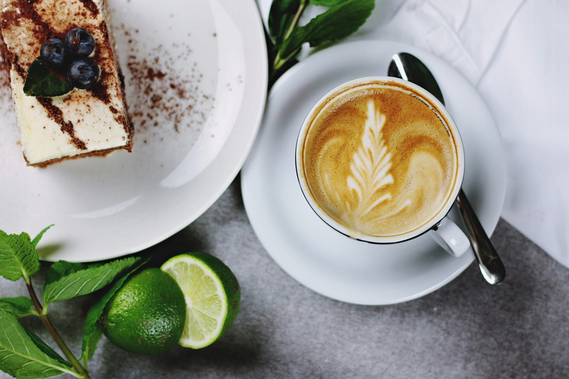 Una taza de café con arte latte junto a un plato con un pastel decorado con moras azules.
