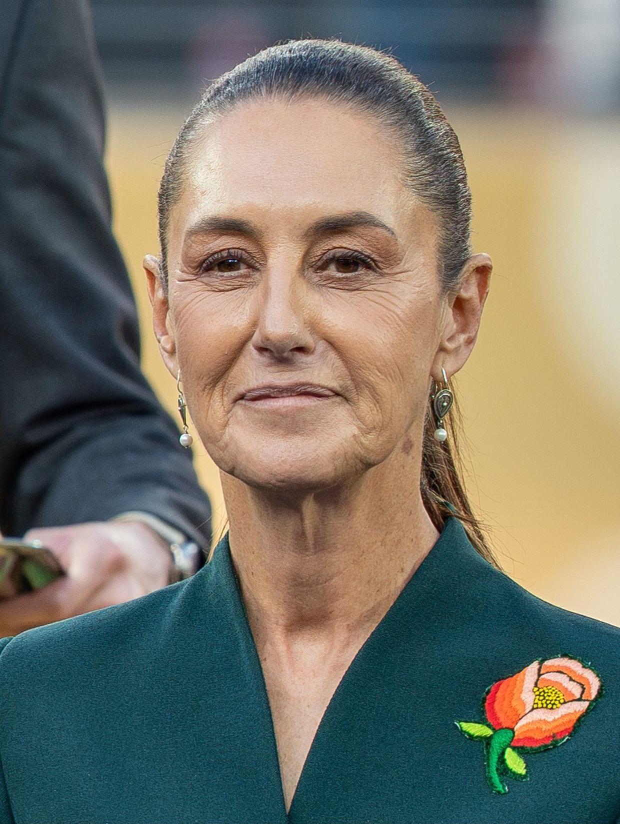 Claudia Sheinbaum posa de cerca en un evento público, con expresión seria y el cabello recogido.