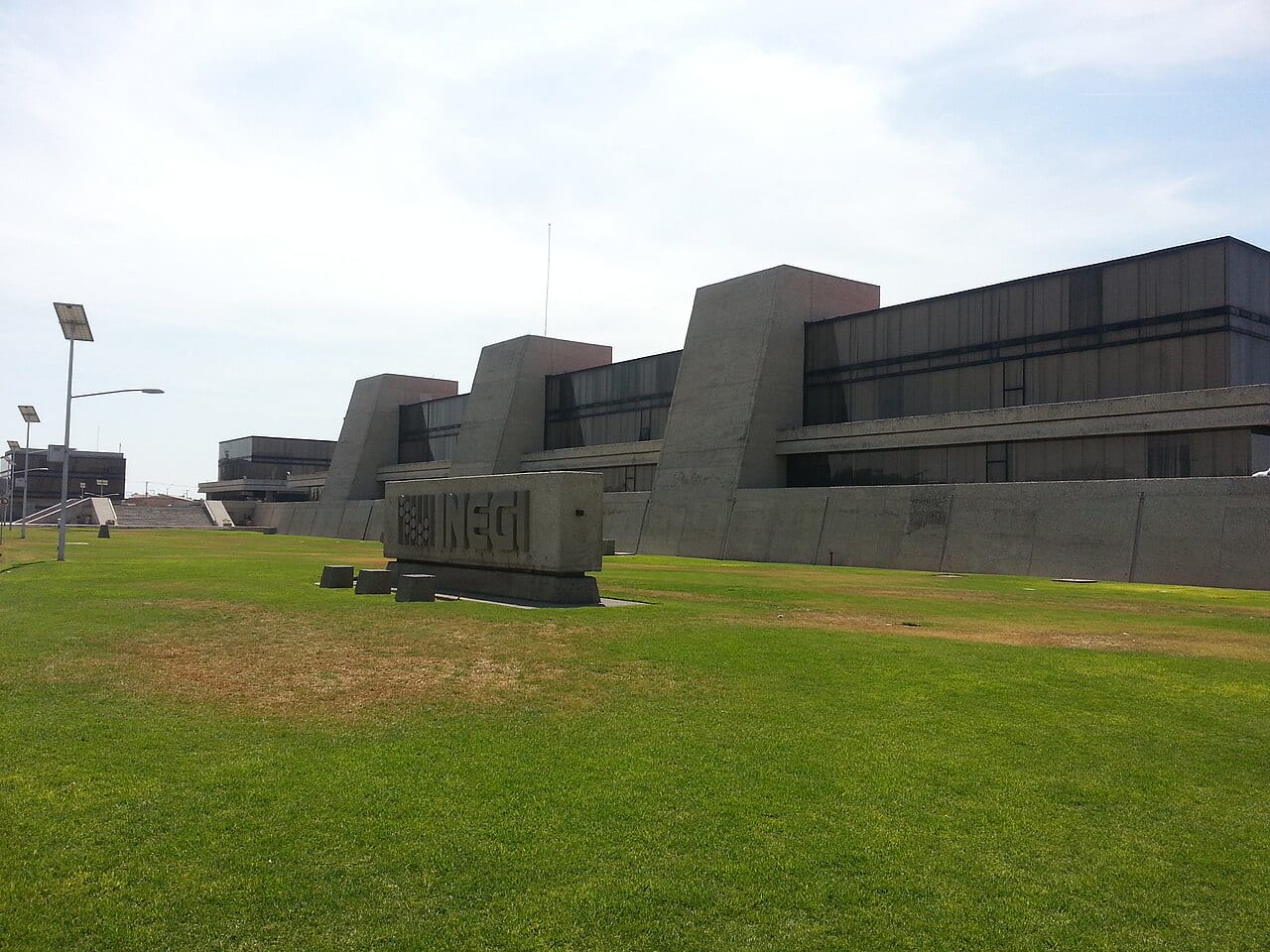 Edificio de concreto con cuerpos triangulares y un letrero de piedra con las siglas INEGI, sobre un jardín.