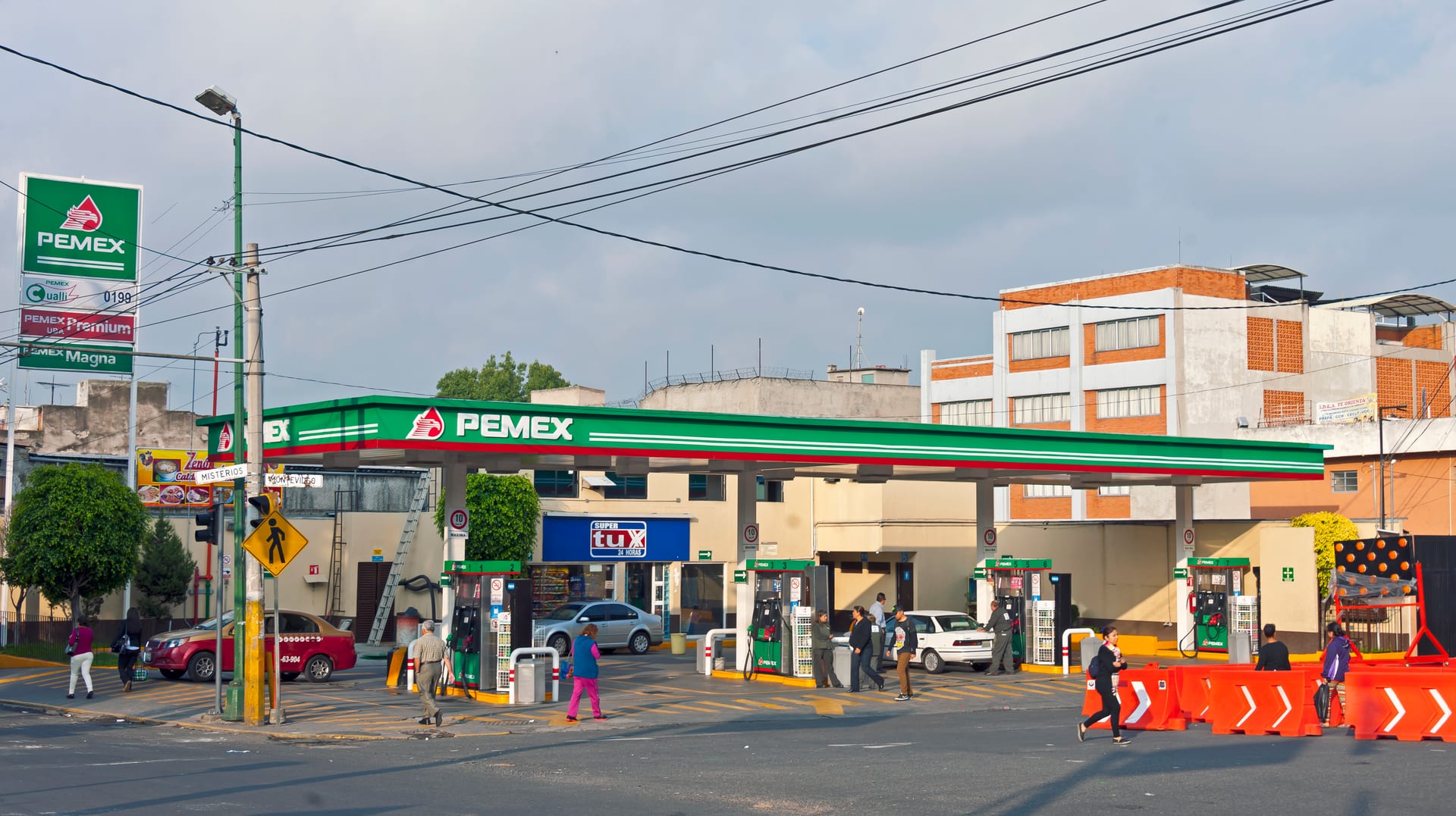 Una estación de servicio Pemex con varias bombas de despacho y clientes caminando junto a la calle.