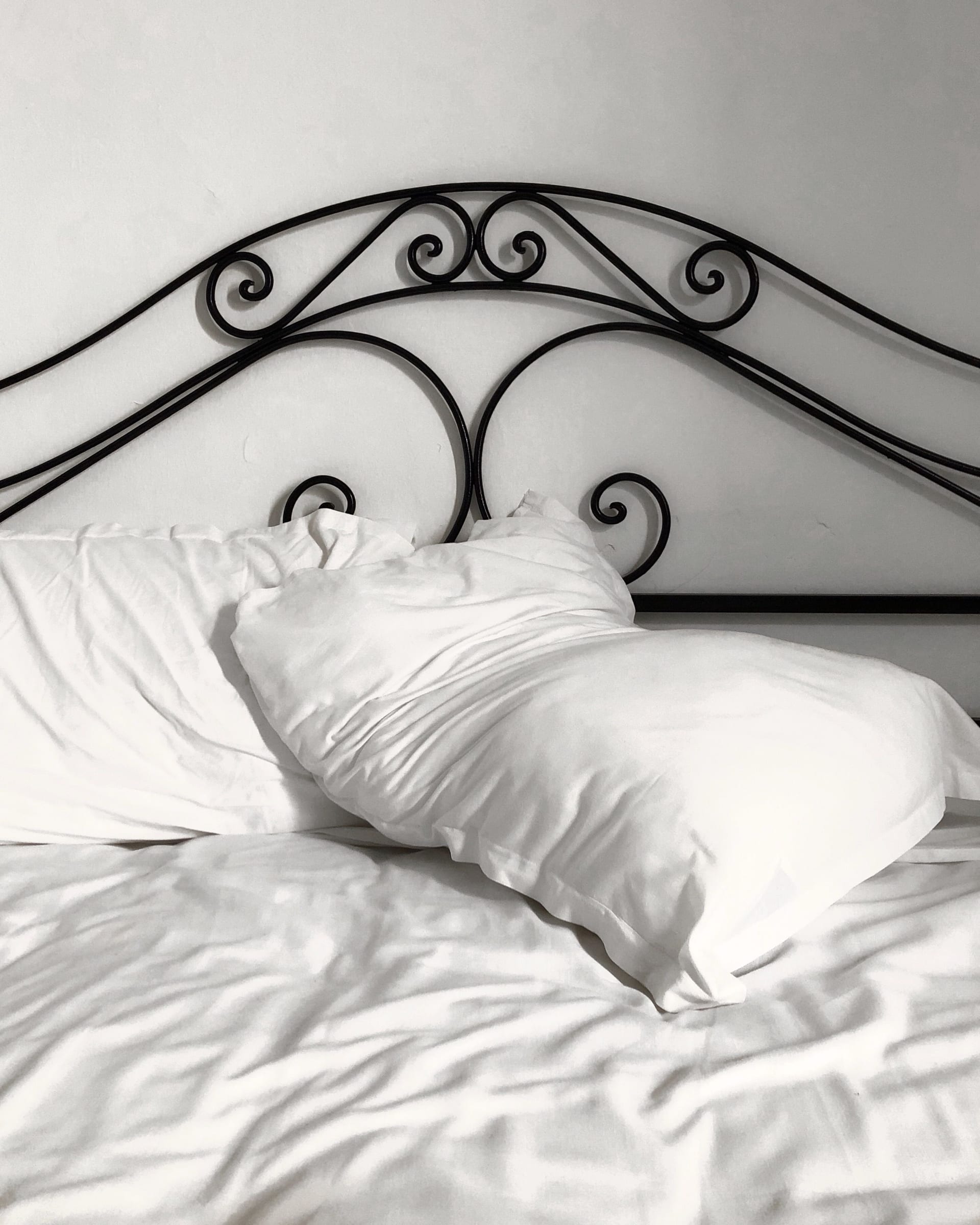 Cabecera de fierro forjado con diseño de espirales sobre una cama tendida con almohadas blancas.