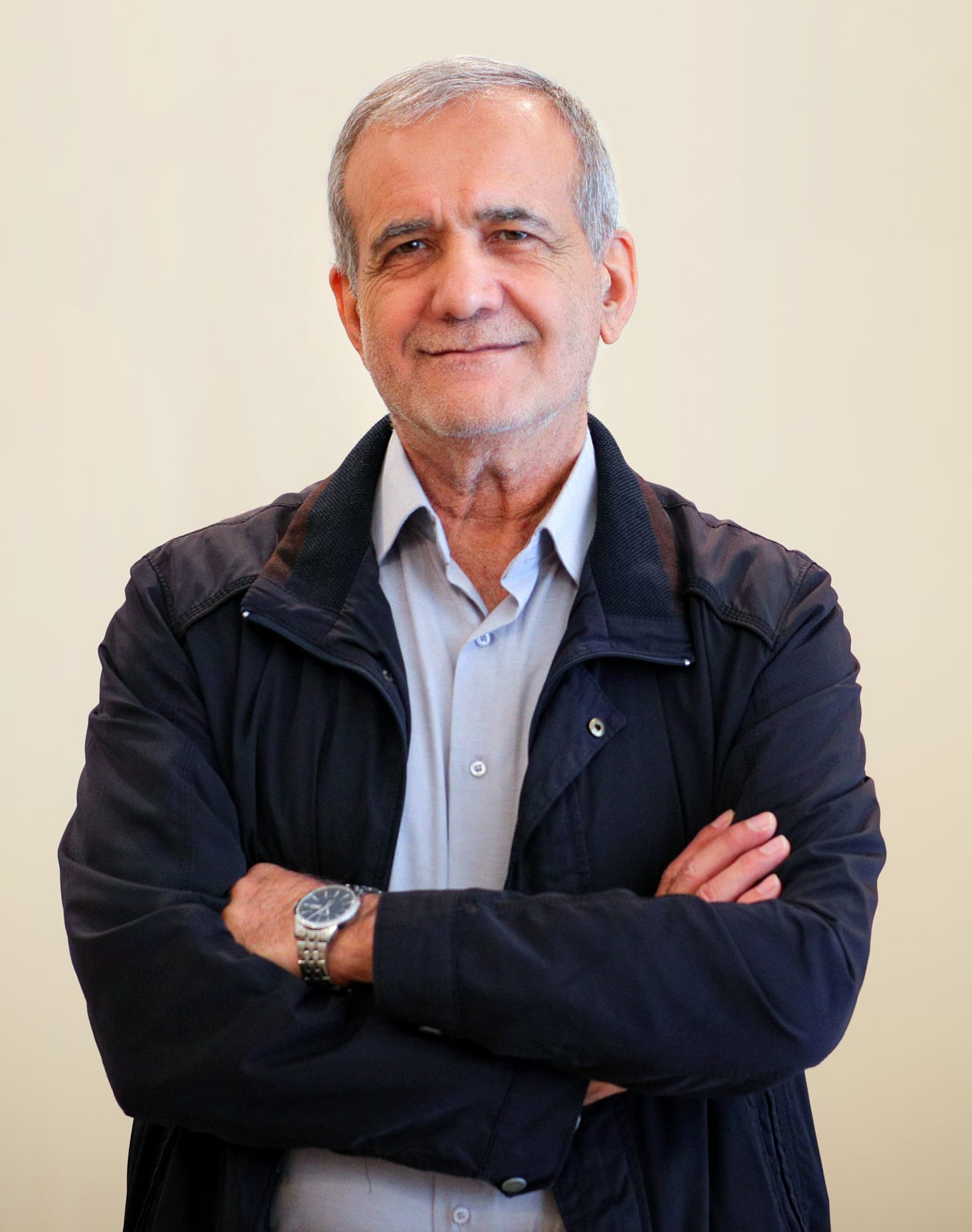 Masoud Pezeshkian con los brazos cruzados, cabello y bigote blancos, vestido con una chamarra oscura sobre camisa clara.
