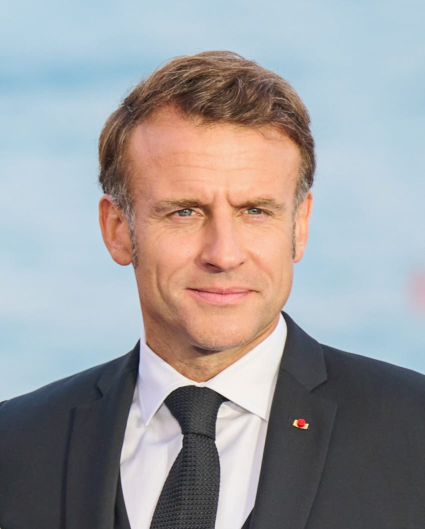 Retrato de Emmanuel Macron con traje oscuro y corbata azul, mirando de frente con gesto serio.