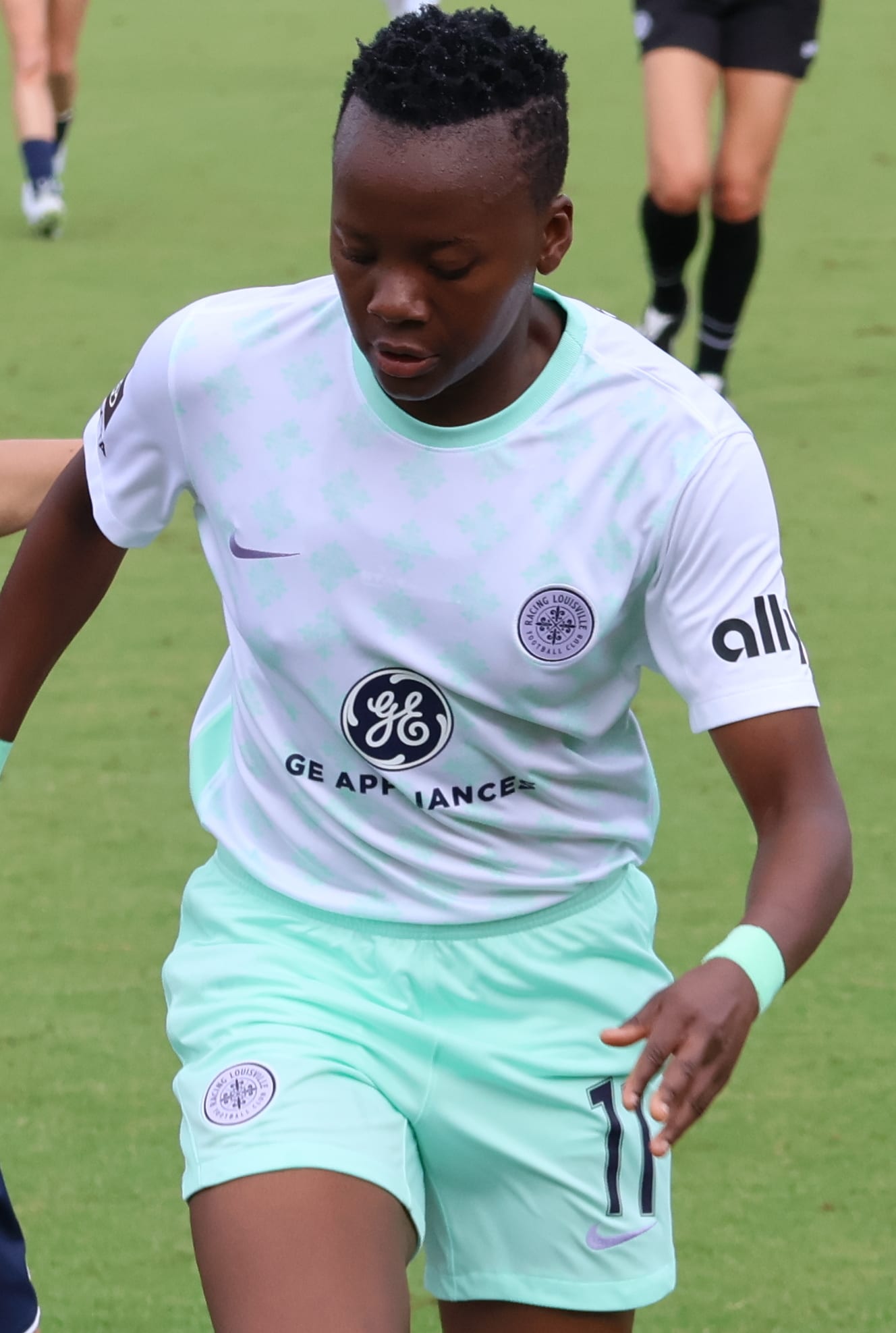 Thembi Kgatlana, con uniforme blanco y verde menta y el número 11, corre por el césped durante un partido. Fotografía de archivo, ajena a este encuentro.