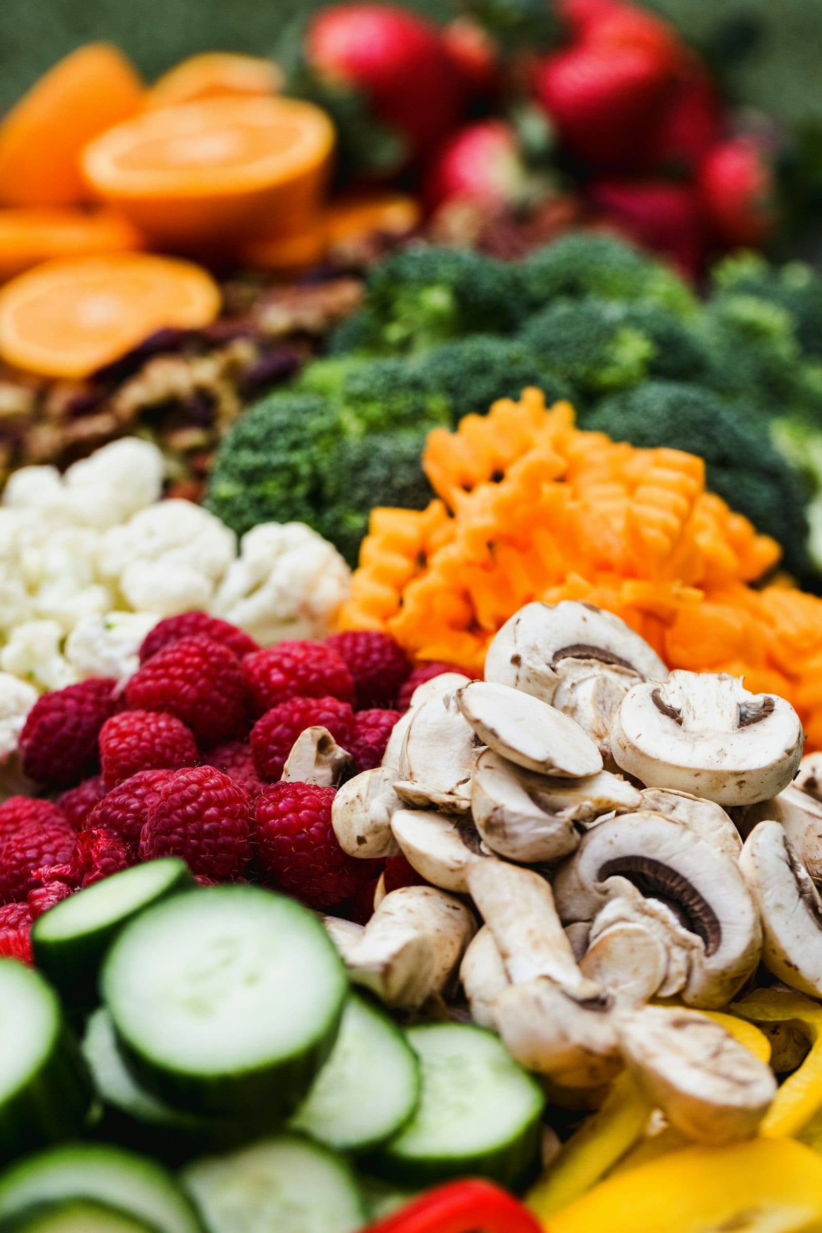 Montones de brócoli, coliflor, zanahoria rallada, champiñones y frambuesas frescas ordenados por color.
