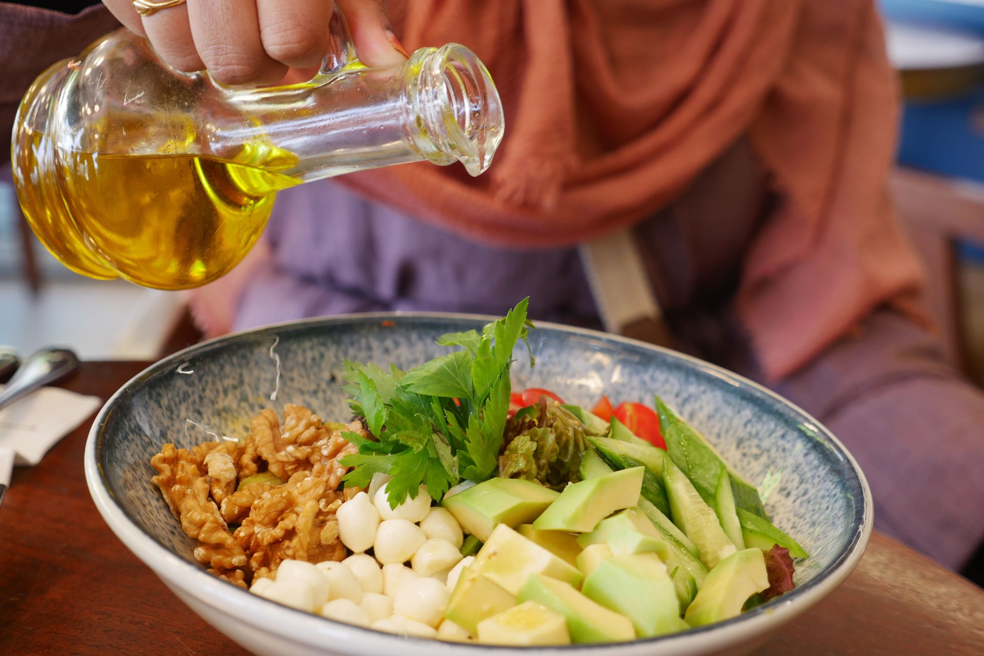 Una mano vierte aceite de oliva sobre una ensalada con nueces, queso y aguacate.