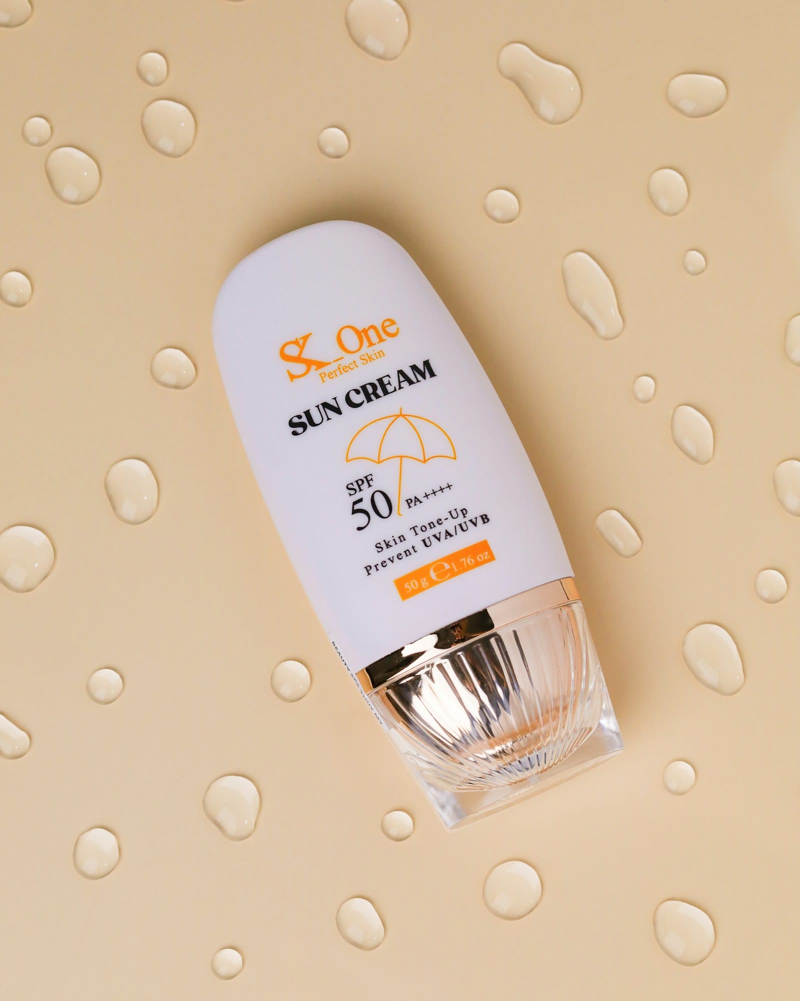 Envase blanco de crema solar con FPS 50 recostado sobre un fondo beige salpicado de gotas de gel.