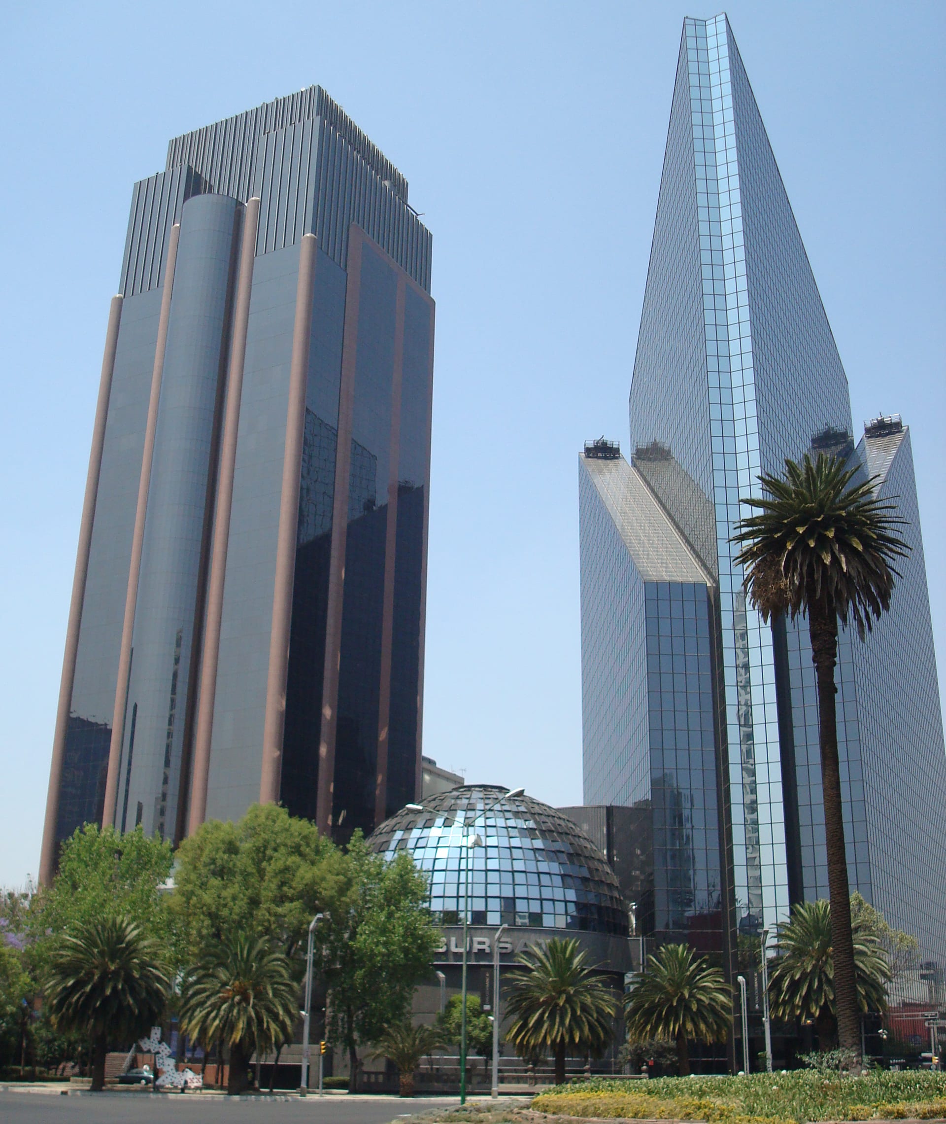 Dos torres de cristal y una cúpula esférica de vidrio, sede de la Bolsa Mexicana de Valores, con palmeras en primer plano.