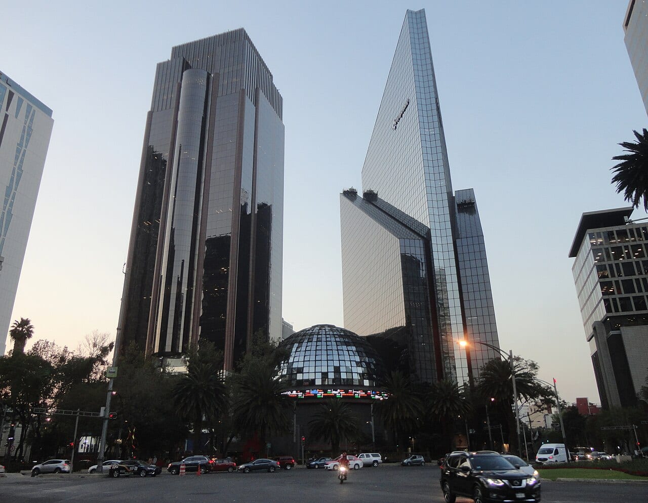La cúpula acristalada de la Bolsa Mexicana de Valores sobre Paseo de la Reforma, con su pantalla de cotizaciones y rascacielos de vidrio detrás al atardecer.