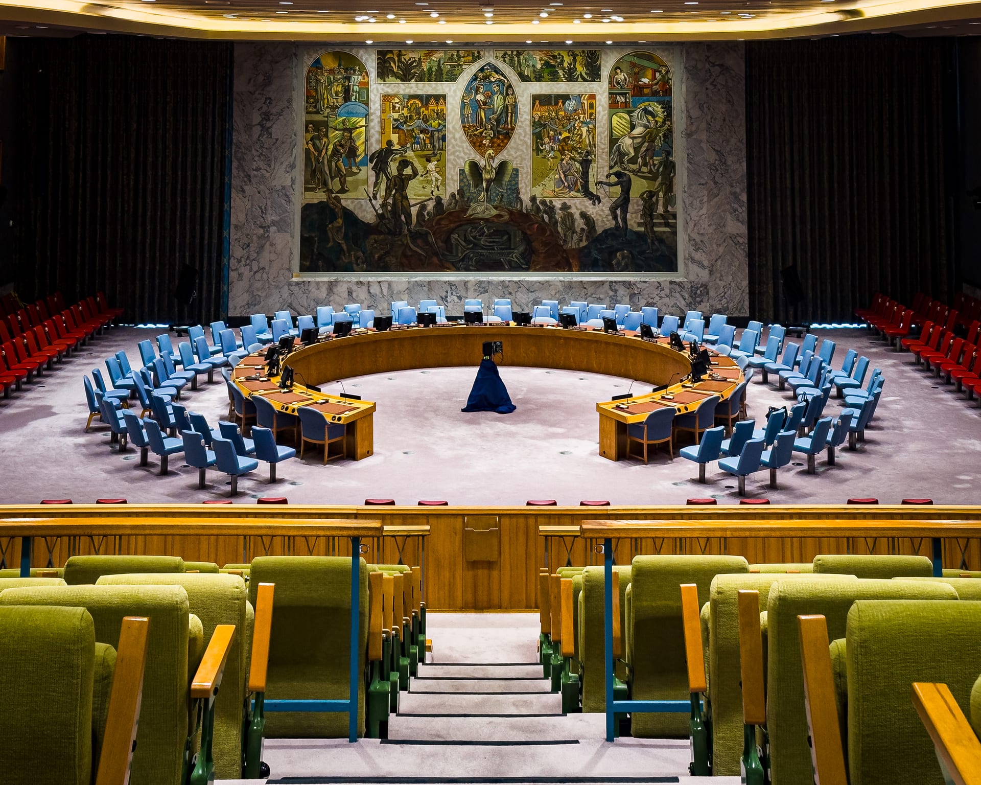 La sala circular y vacía del Consejo de Seguridad de la ONU, con sillas azules alrededor de la mesa en herradura y un mural al fondo.