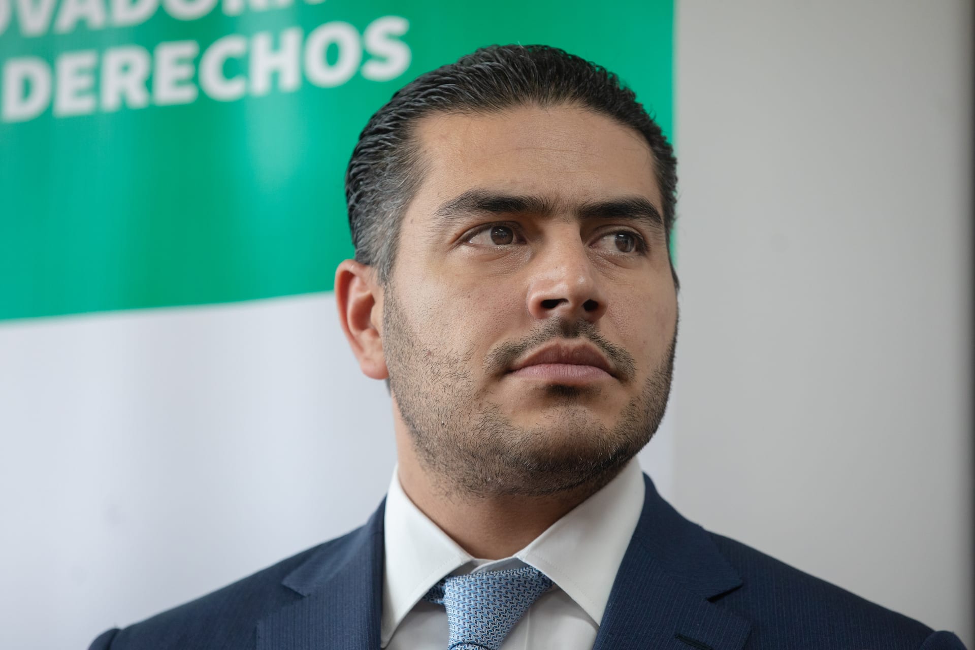 Omar García Harfuch, de traje oscuro y corbata, con gesto serio frente a un cartel institucional.