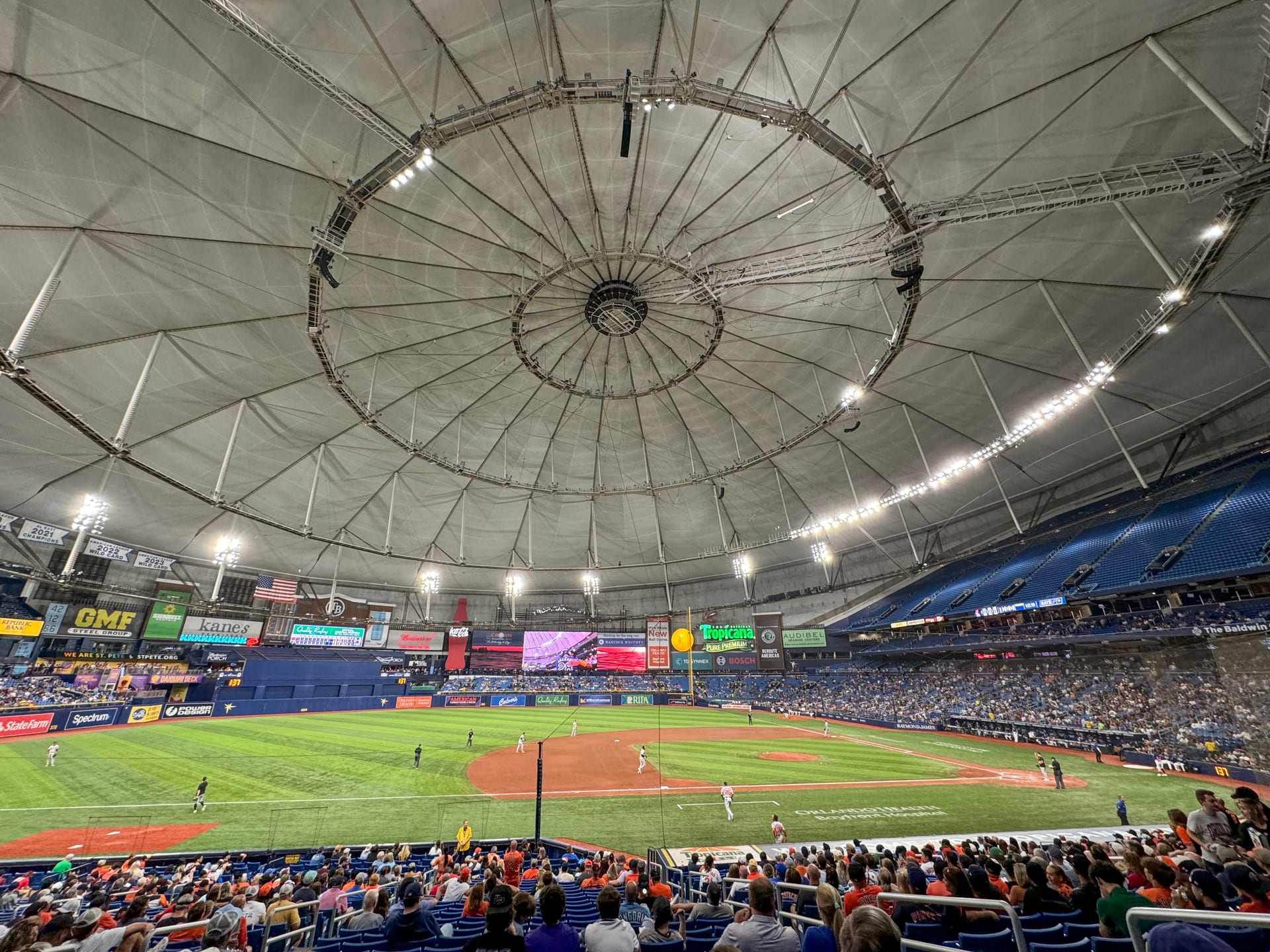 Interior del Tropicana Field bajo su techo domo, con el campo iluminado y las gradas llenas de aficionados durante un juego.