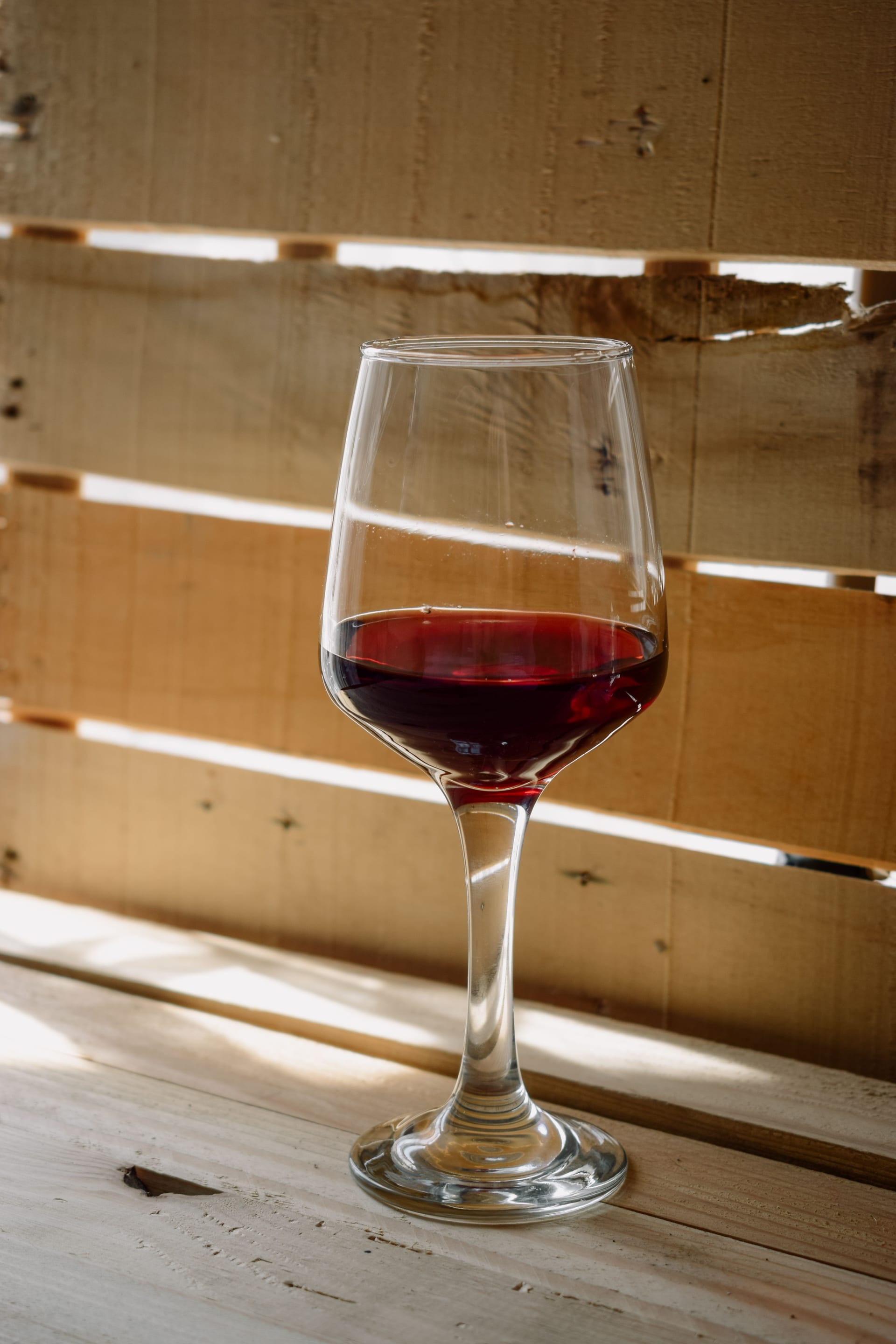 Copa de vino tinto servida hasta una cuarta parte sobre una mesa de madera, con tablones claros de fondo.