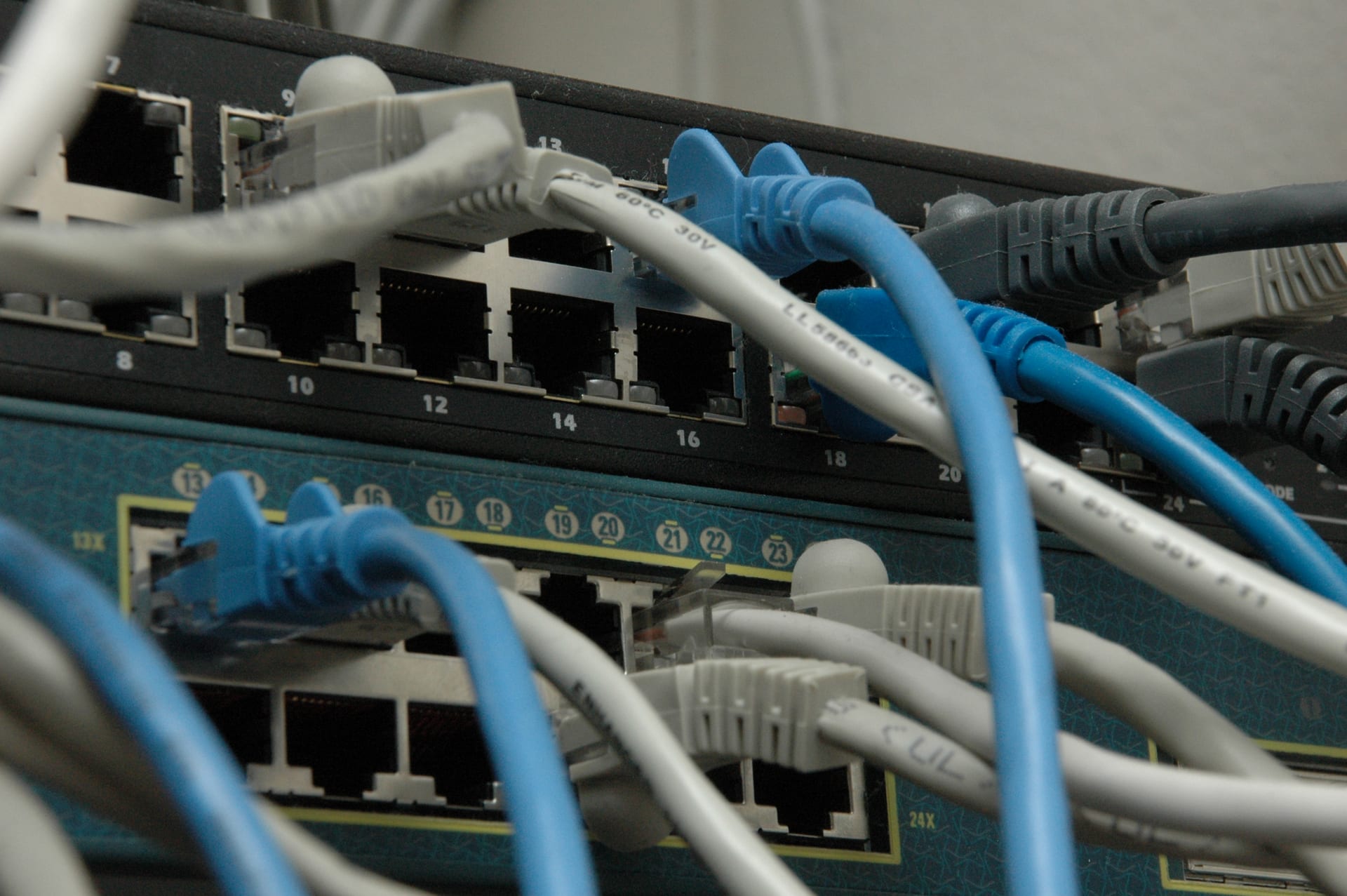 Primer plano de dos switches de red apilados, con varios cables de red grises y azules conectados a sus puertos numerados.