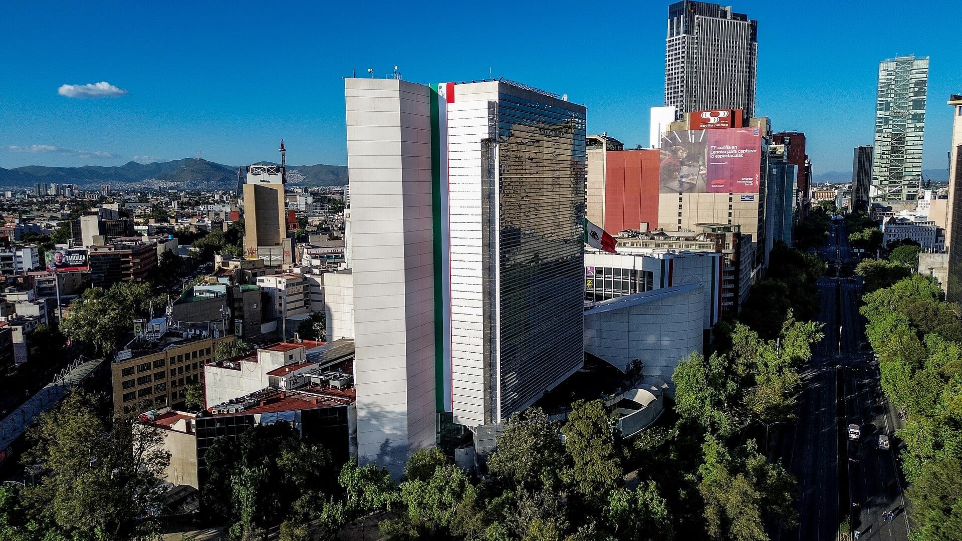 Vista aérea de una torre de cristal en Ciudad de México con un gran mural de la bandera mexicana en su fachada.
