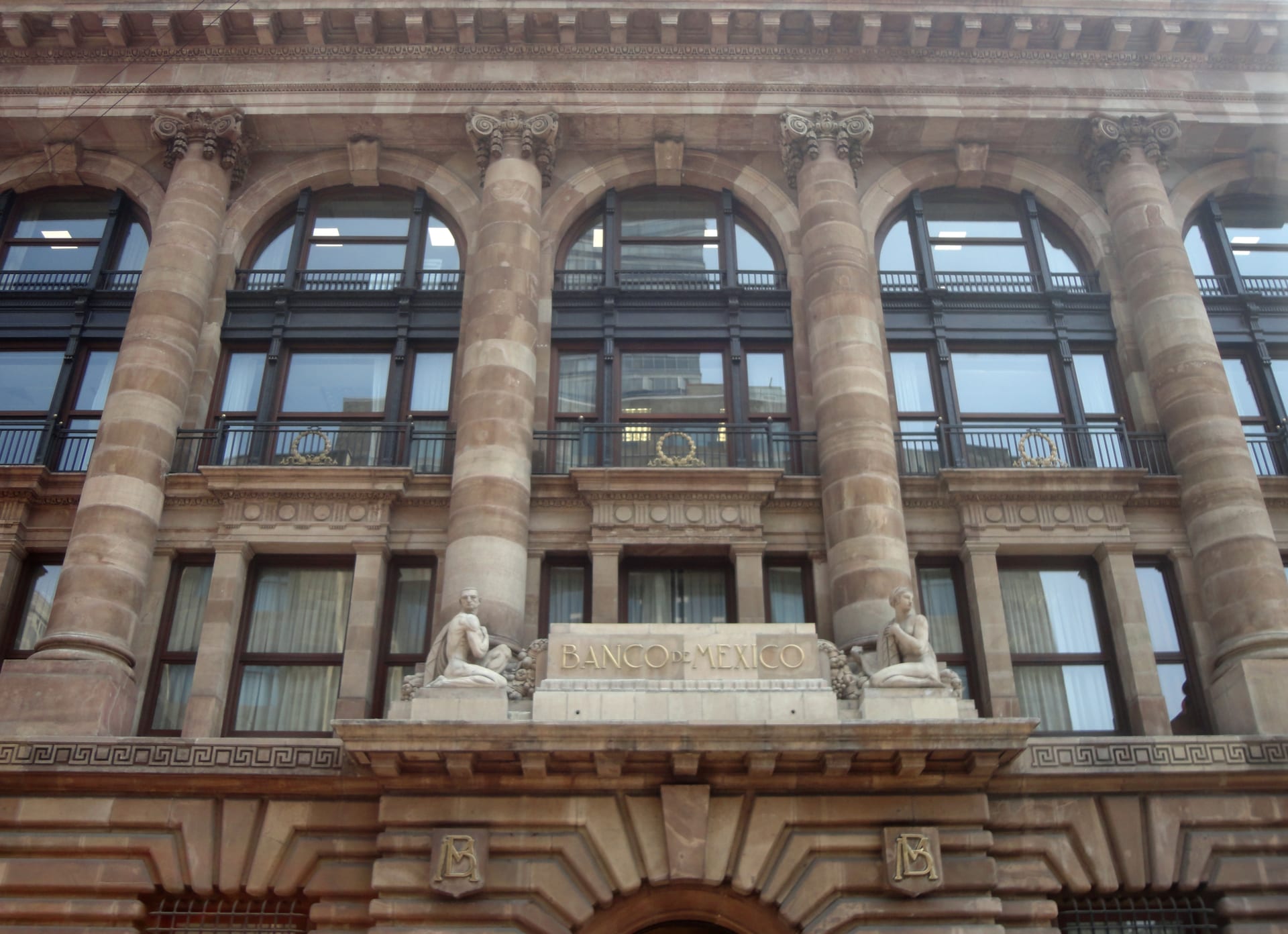 Fachada neoclásica de un edificio con columnas de piedra y el emblema circular del Banco de México sobre la entrada.