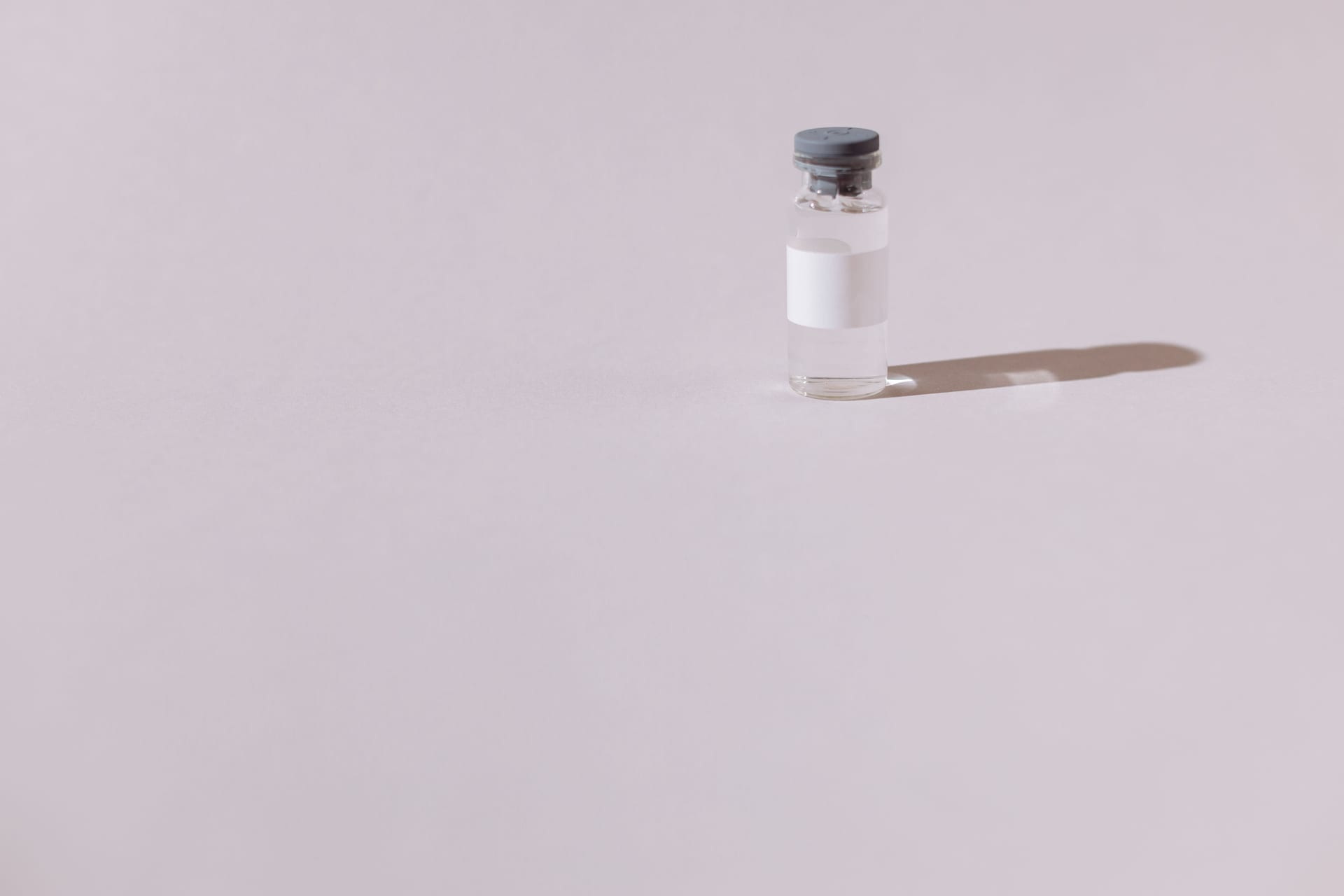 Un frasco de vacuna estéril y sellado, aislado sobre un fondo gris liso.