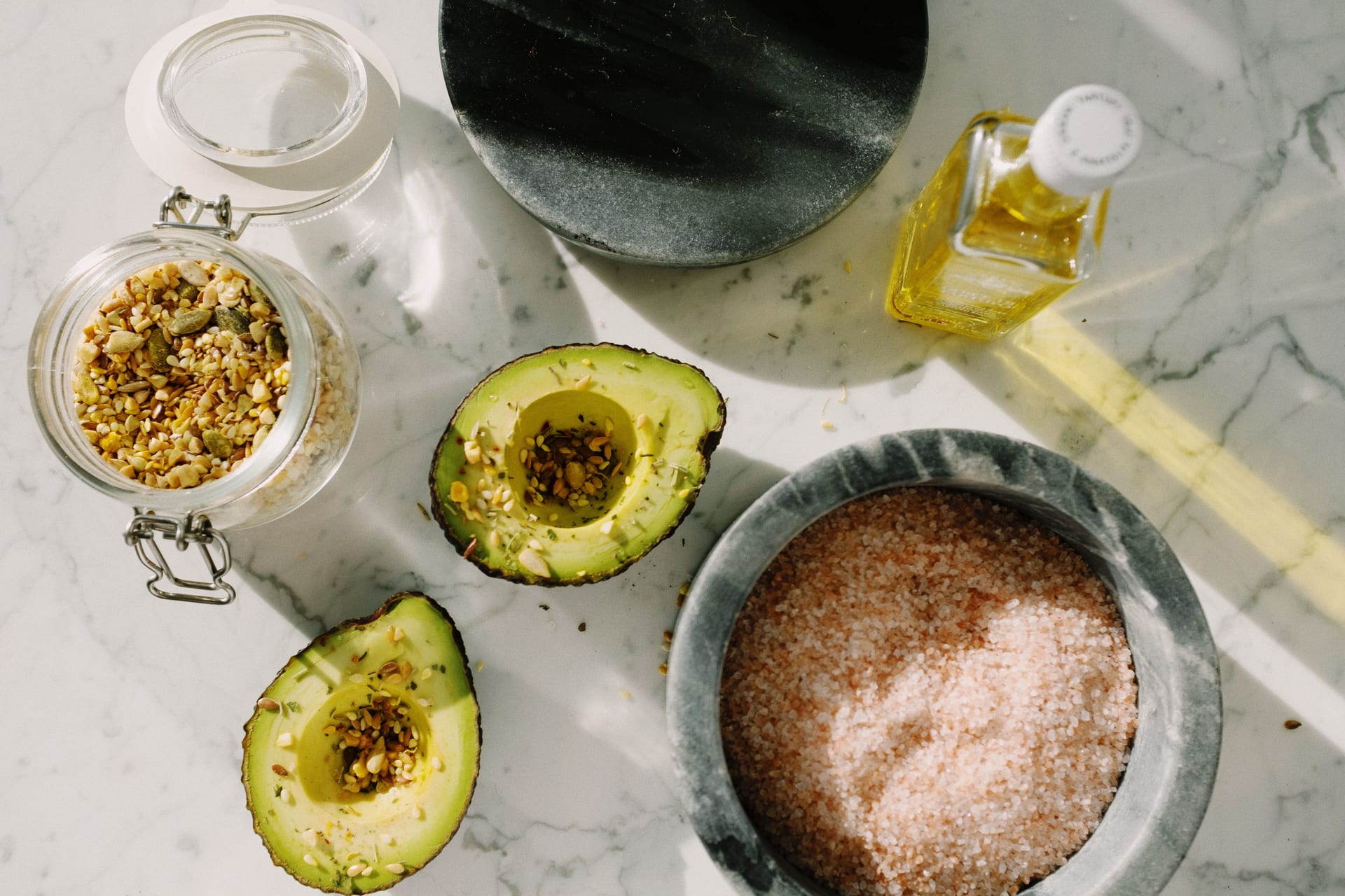 Un aguacate partido a la mitad y relleno de semillas, junto a un plato con sal rosa.
