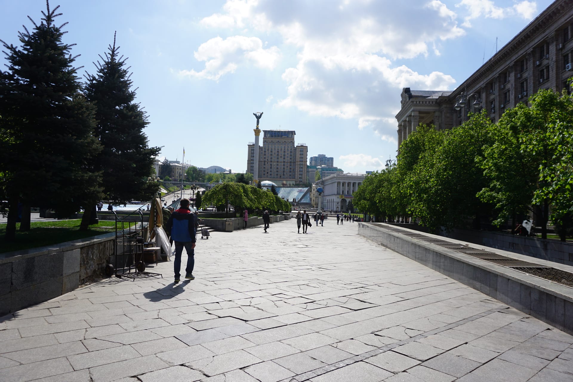 Plaza pública de Kiev con el Monumento a la Independencia al fondo; varias personas caminan bajo un cielo despejado.