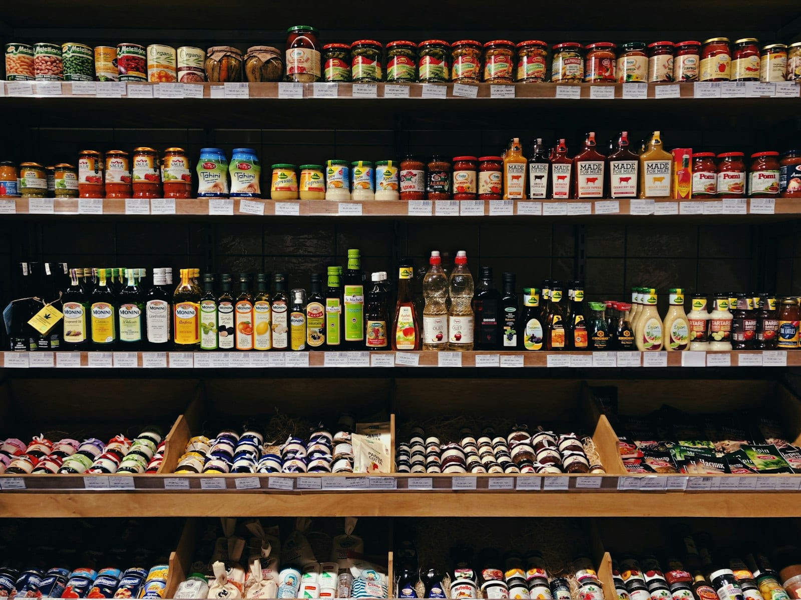 Anaqueles de supermercado con hileras de frascos y botellas de salsas, aceites y condimentos con distintas etiquetas.