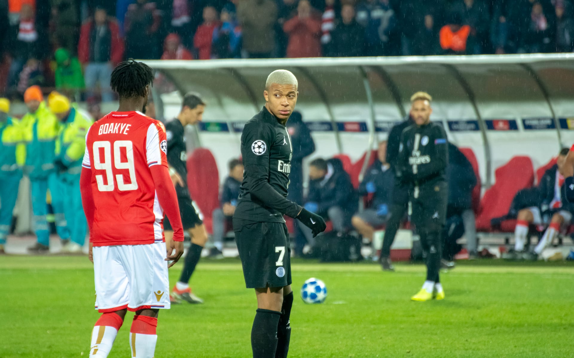 Kylian Mbappé, con playera negra y el número 7, mira hacia un lado durante un partido, con el balón en el césped junto a él.