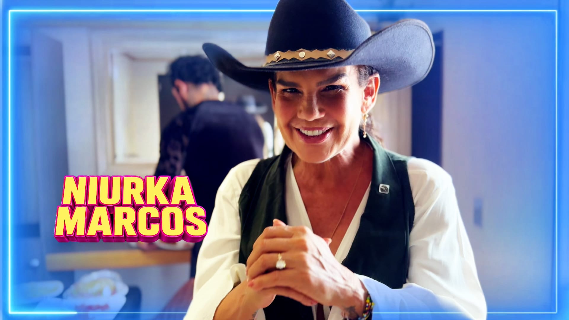 Niurka Marcos sonríe con sombrero vaquero negro y chaleco verde, con las manos entrelazadas frente al pecho.
