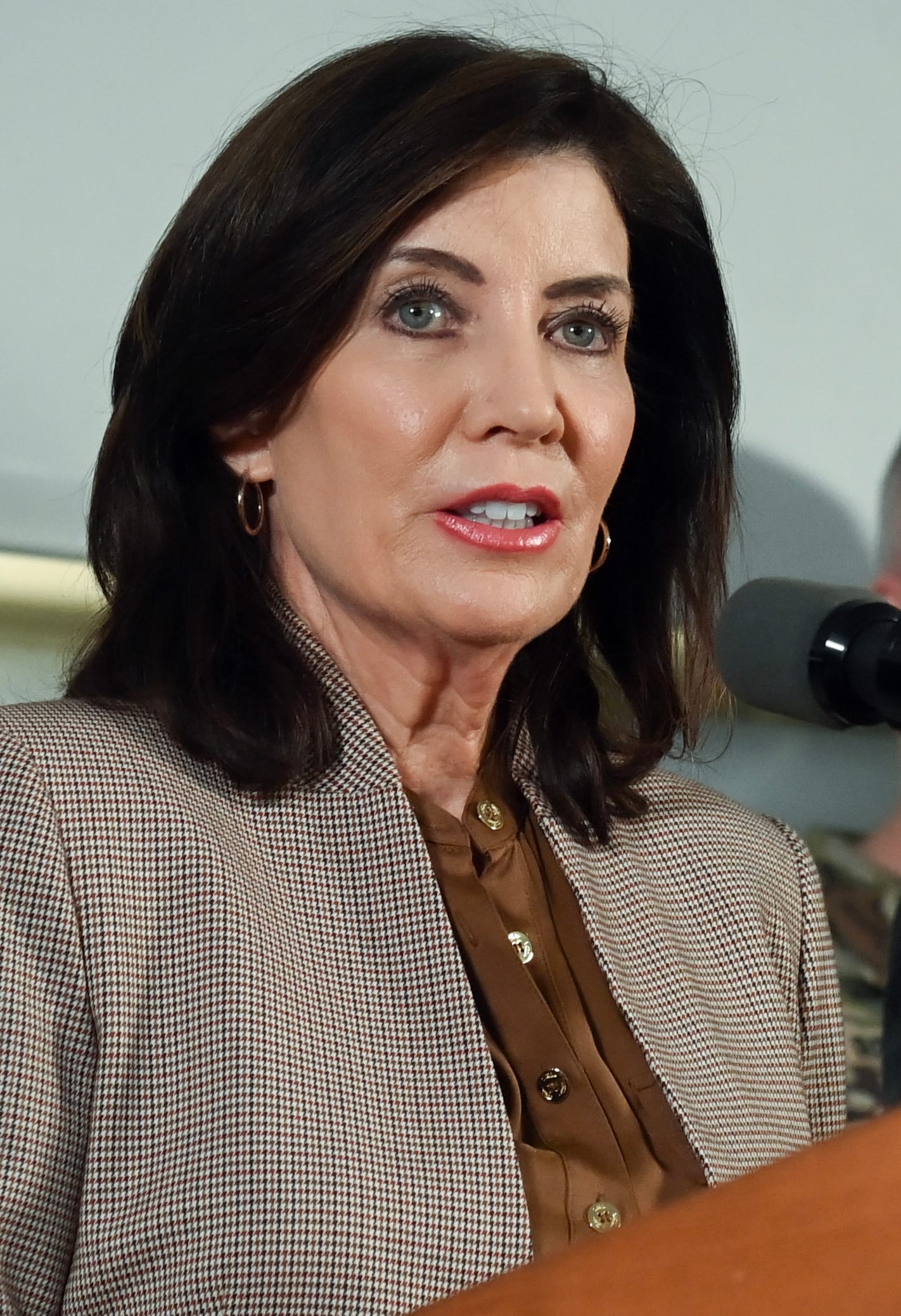 Kathy Hochul habla en un podio junto a un hombre, dentro de un centro de control con pantallas al fondo.